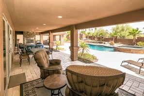 A covered patio area with outdoor furniture, a pool, and a stone fireplace.