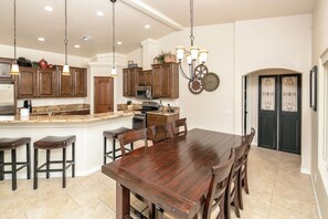 A kitchen with wooden cabinets, a central island, bar stools, a dining table, and pendant lighting.