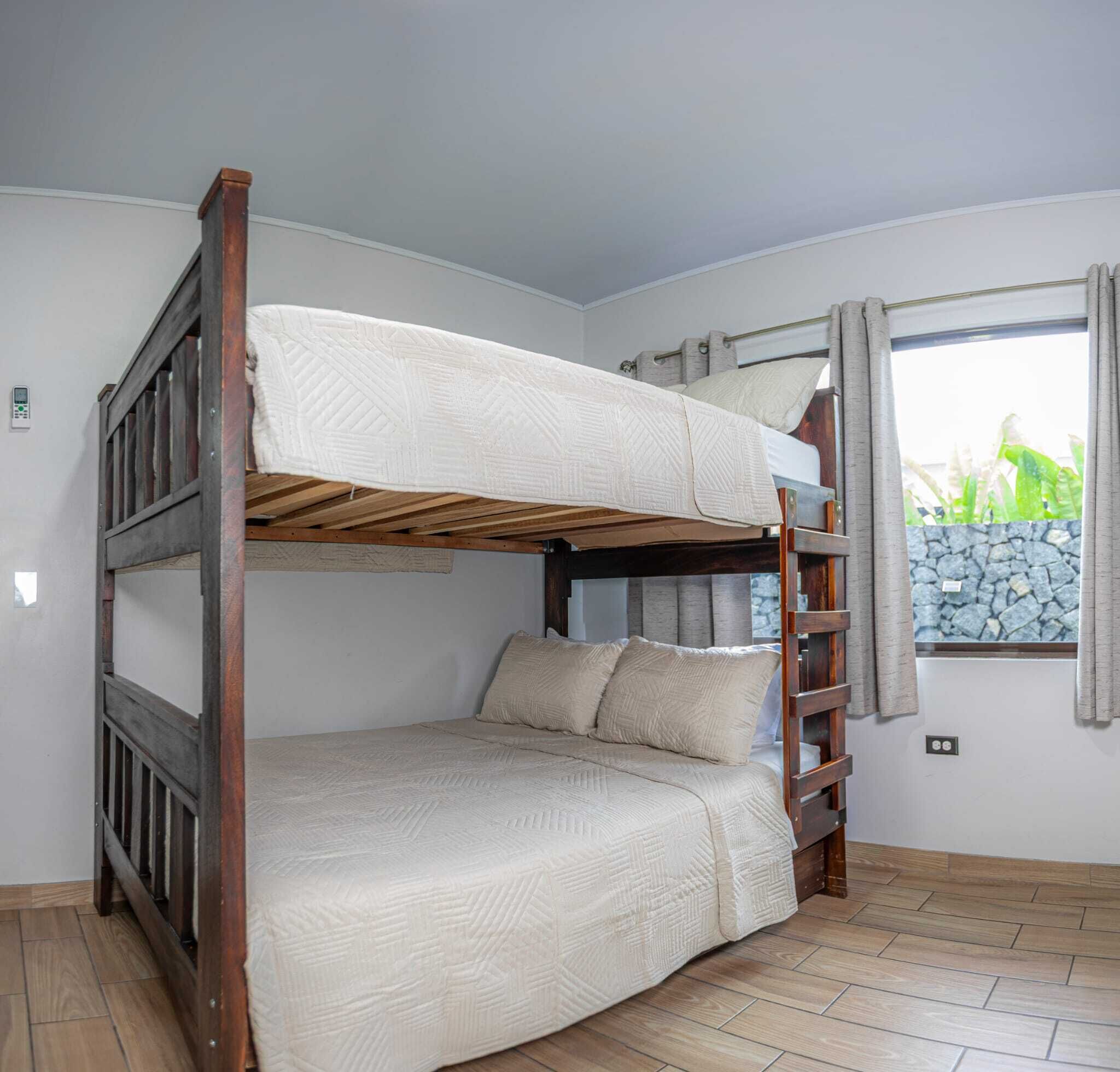 Une chambre avec un lit superposé, une structure en bois, un matelas blanc et une fenêtre avec des rideaux.