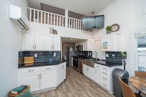 A modern kitchen with white cabinets, black countertops, and a TV mounted above the stove.