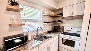 A compact kitchen with a built-in microwave, a sink, and a stove. There are white cabinets and a granite countertop. - Miami Art Deco Vibes • Stay Near Downtown (Tampa)