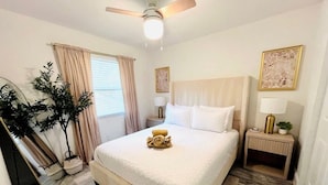 A neatly arranged bedroom with a large bed, a ceiling fan, a bedside table with a lamp, and a mirror. - Miami Art Deco Vibes • Stay Near Downtown (Tampa)