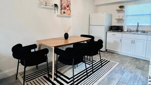 A modern kitchen with white cabinets, a refrigerator, and a microwave. There is a dining table with black chairs and a black and white striped rug. - Miami Art Deco Vibes • Stay Near Downtown (Tampa)
