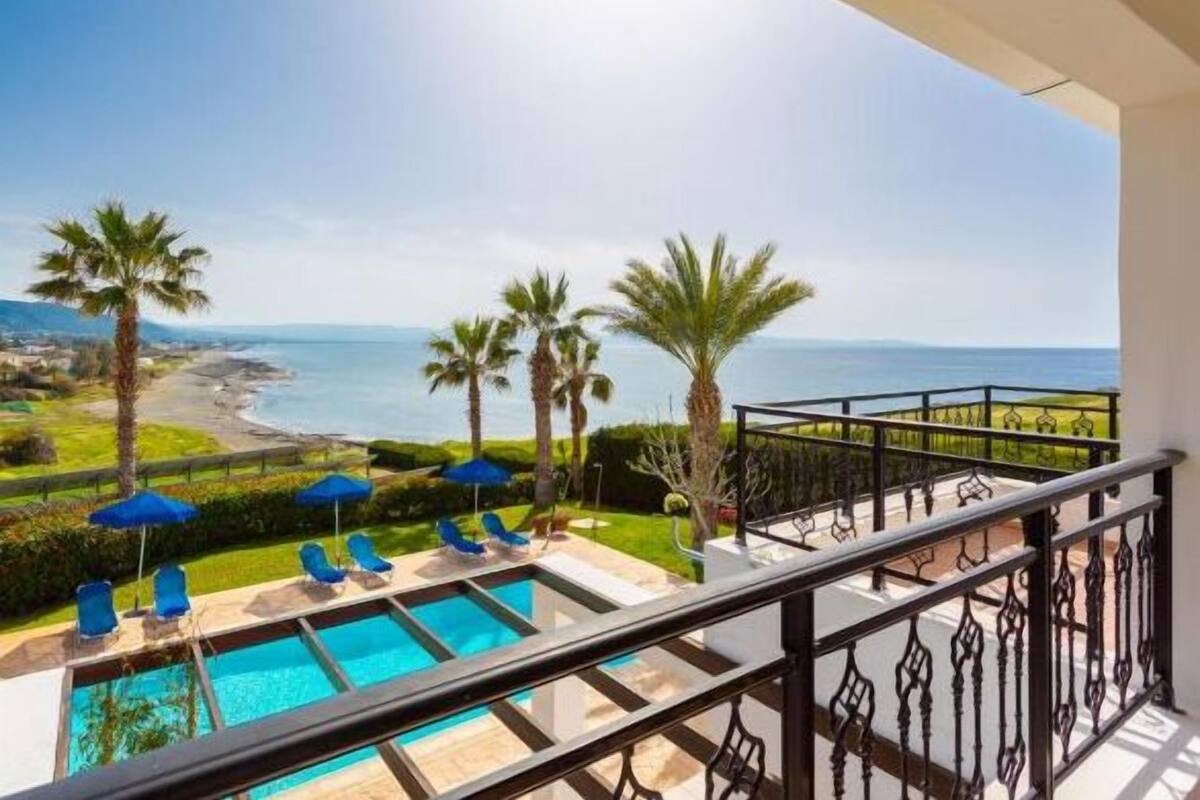 A balcony with a pool, blue umbrellas, and a view of the sea and beach.