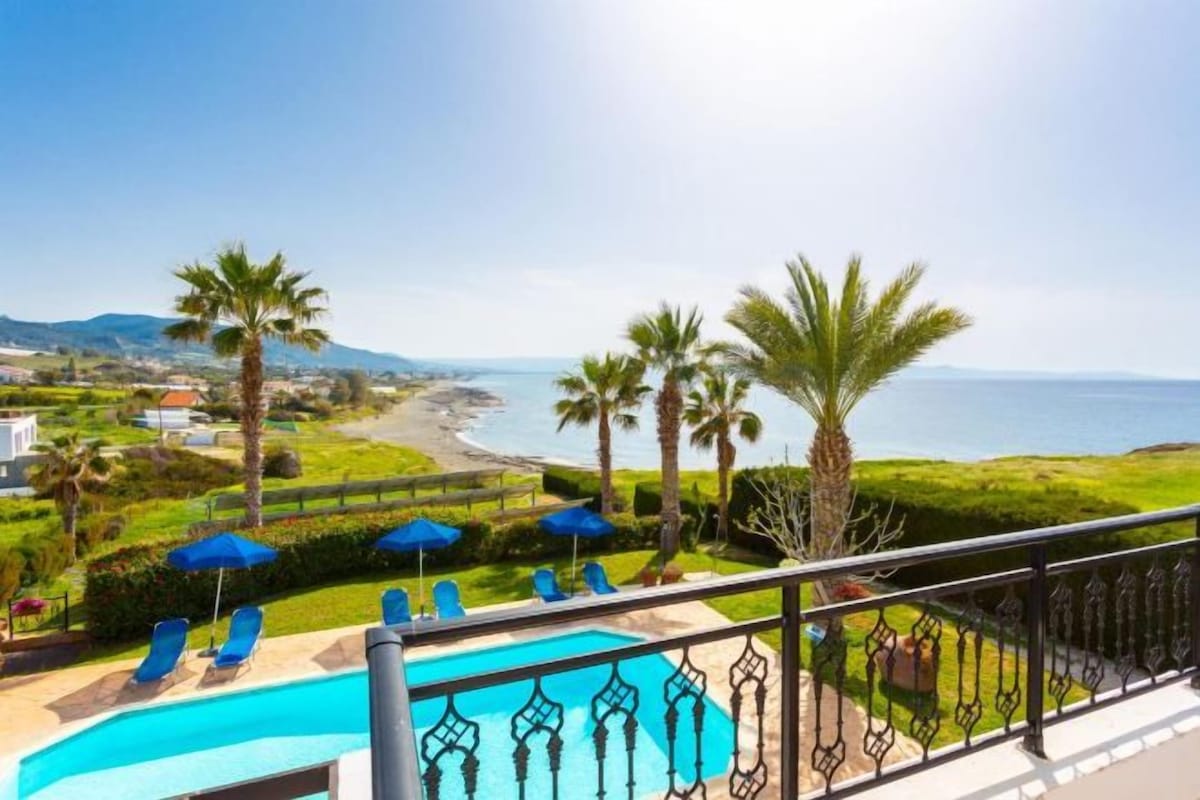 A pool area with lounge chairs and umbrellas, overlooking a beach and ocean.