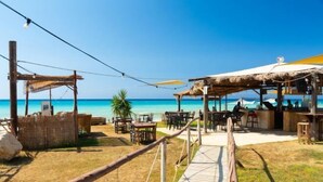 A beachside restaurant with outdoor seating, a wooden deck, and a view of the ocean. - Villa Pelagos (Nea Dimmata)