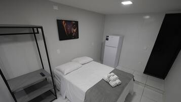 Un dormitorio con cama, una mesita, un refrigerador y un separador negro.