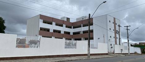 A multi-story parking garage with white walls and brown accents, adjacent to a road with a sidewalk.