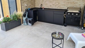 Una cocina exterior compacta con una parrilla integrada, un lavabo y una pequeña mesa.