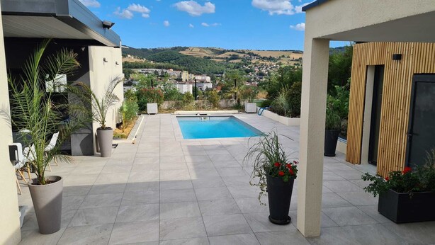 Una terraza en la azotea con piscina, plantas en macetas y vistas a un pueblo lejano.