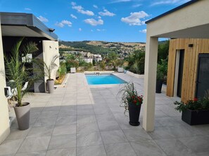 A rooftop patio with a swimming pool, potted plants, and a view of a town in the distance. - Villa with Private Pool & Cinema Room (La Ricamarie)