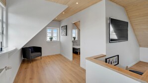 A modern interior with a sloped ceiling, wooden floors, a black chair, and a large TV mounted on the wall. - 3 bedroom amazing home in Sydals (Sydals)