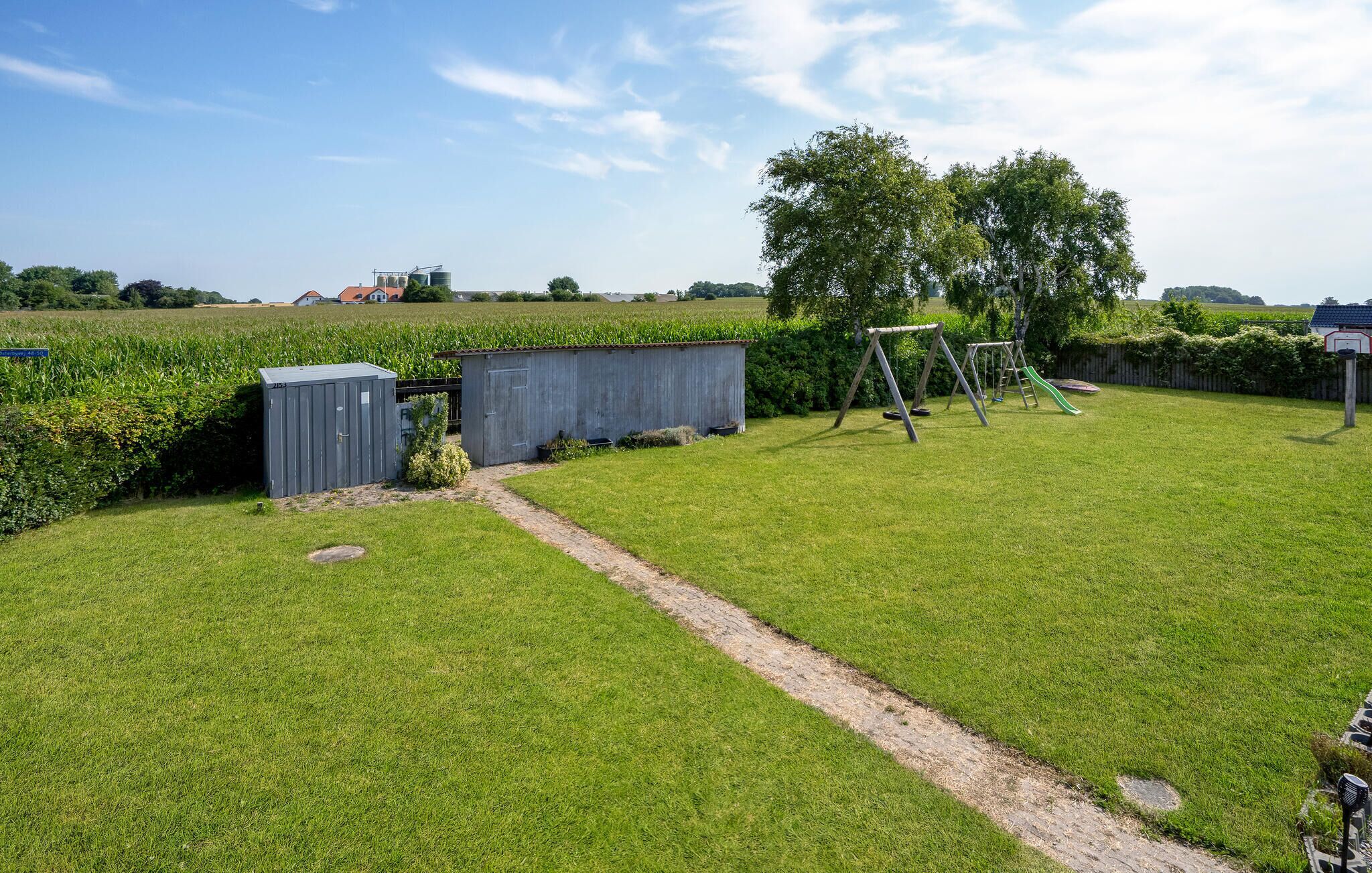 A well-maintained grassy yard with a swing set, a small shed, and a paved path.