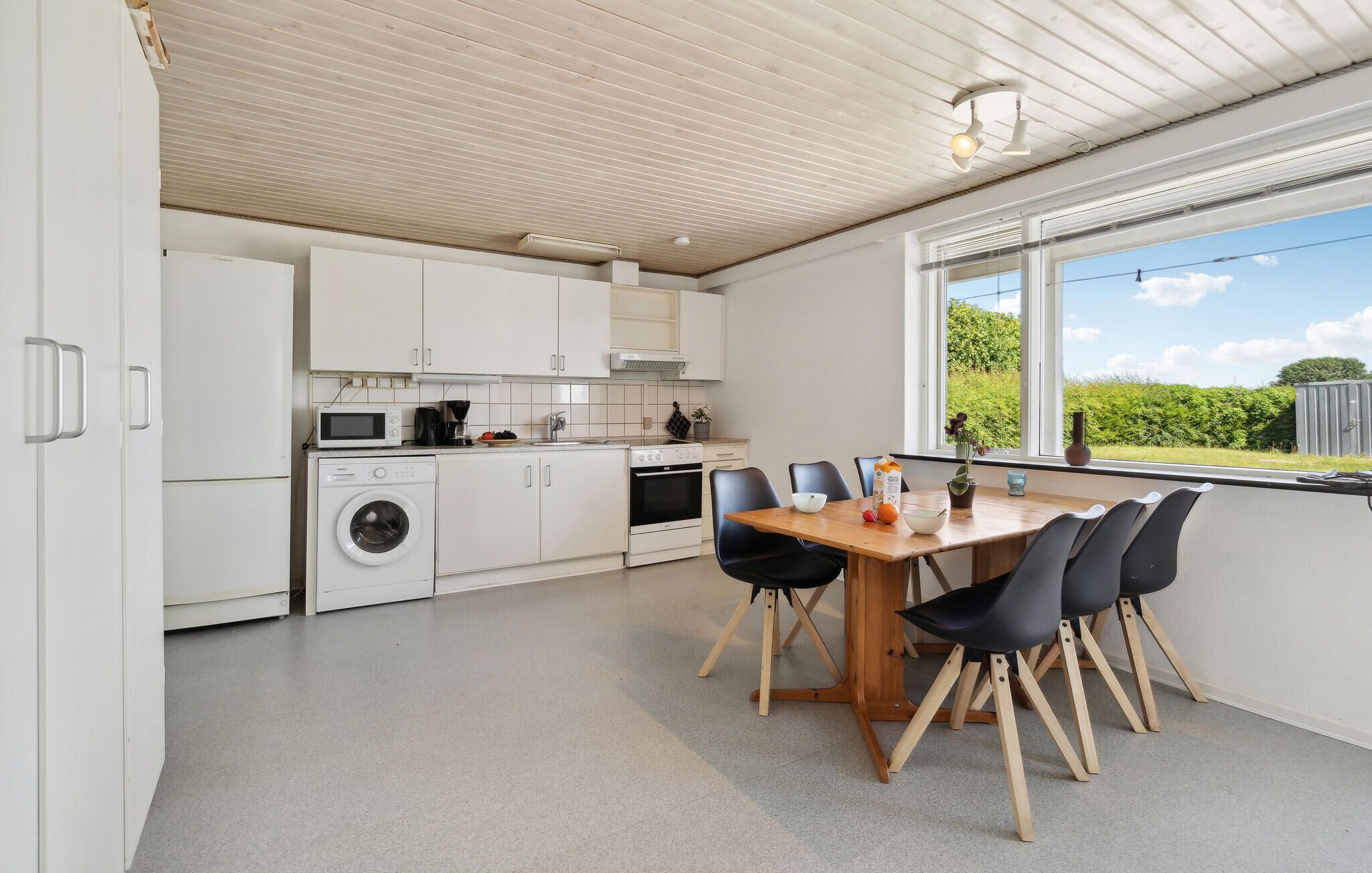 A modern kitchen with white cabinetry, a dining table with chairs, and a view of greenery outside.