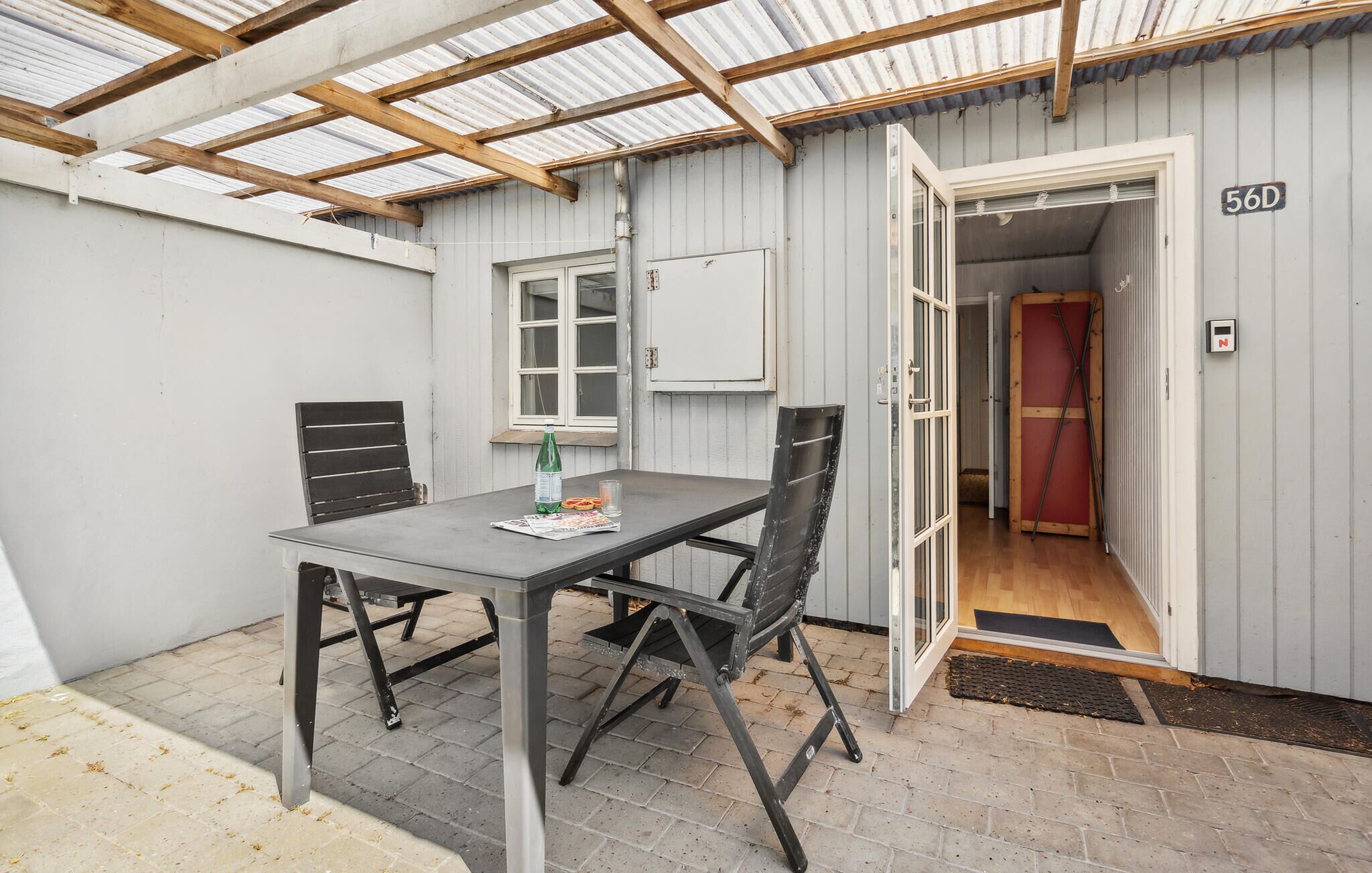 A covered patio with a table and chairs, a window, and a door leading to an interior space.