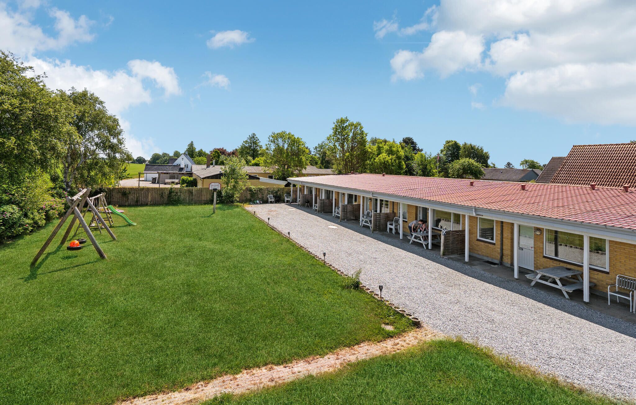 A hotel with a covered outdoor seating area, a grassy lawn, and a playground.