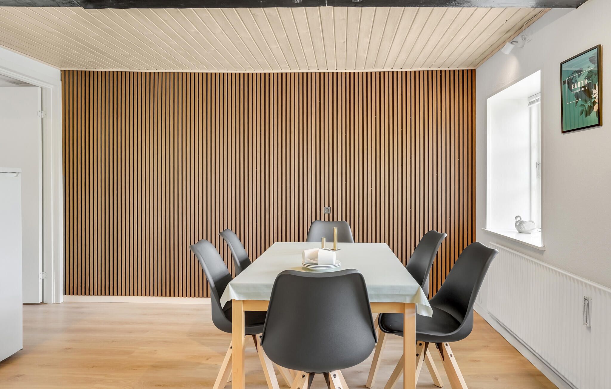 A dining area with a wooden slatted wall, a white table, and black chairs.