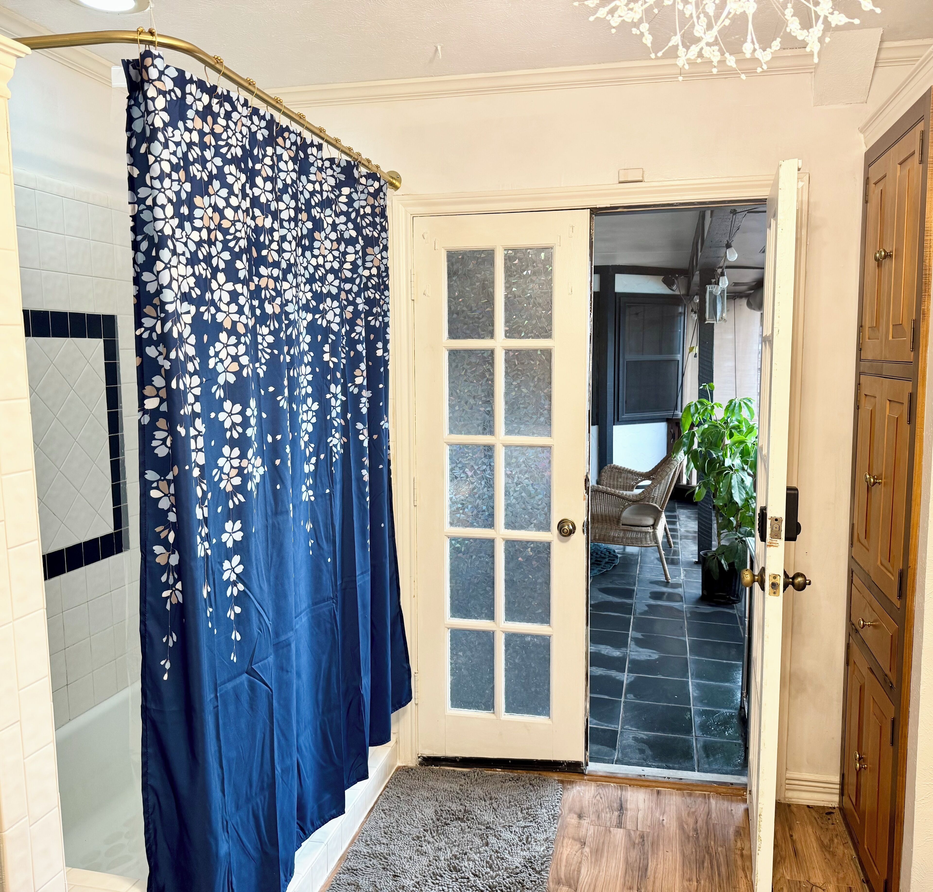 A bathroom with a shower curtain, a glass door, a wooden door, and a rug.
