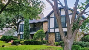A two-story house with a balcony, surrounded by trees and a well-maintained lawn. - Cozy Pool Home Designed for Both Family Fun & Serenity (Plano)