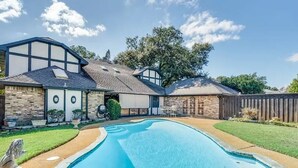 A backyard with a swimming pool, stone walls, and a wooden fence. - Cozy Pool Home Designed for Both Family Fun & Serenity (Plano)