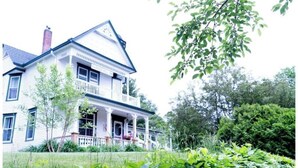 A two-story house with a porch, surrounded by greenery. - Harbor Hill Inn - Penzance Suite (Pepin)