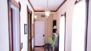 A hallway with wooden flooring, a chandelier, a potted plant, and a staircase with a patterned carpet. - Harbor Hill Inn - Penzance Suite (Pepin)