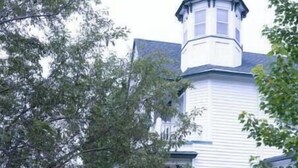 A white building with a turret and a covered patio area with metal chairs. - Harbor Hill Inn - Penzance Suite (Pepin)