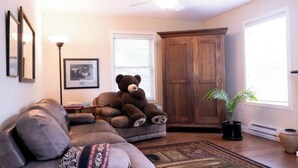 A cozy living room with a sectional sofa, a large wooden cabinet, a floor lamp, and a potted plant. - Harbor Hill Inn - Carriage House (Pepin)