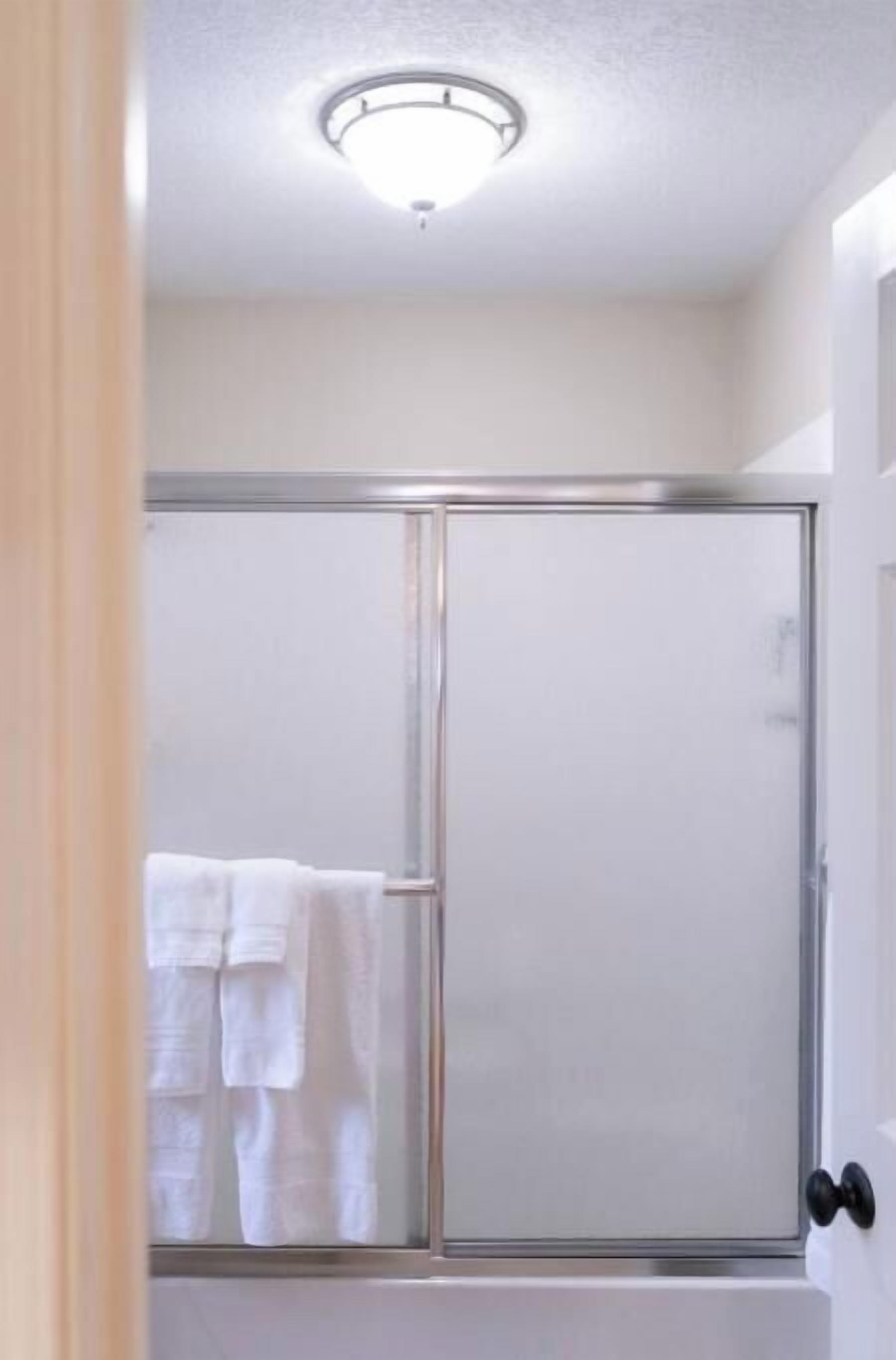 A bathroom with a glass shower enclosure, a white towel rack, and a door with a black handle.