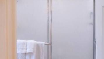 A bathroom with a glass shower enclosure, a white towel rack, and a door with a black handle.