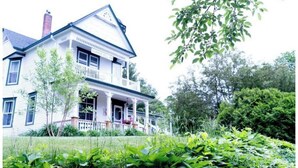 Een tweelaags huis met een veranda, omgeven door groen.