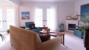 Una sala de estar con sofá color beige, un sillón azul, una mesa de centro de madera y una chimenea.