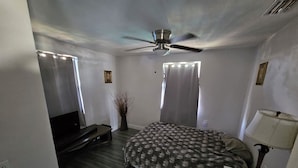 Un dormitorio con cama, televisor, ventilador de techo y lámpara.