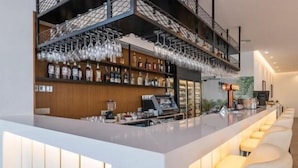 A modern bar area with a long counter, multiple shelves of liquor bottles, and hanging wine glasses.