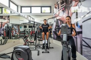 Un gimnasio con equipo de ejercicio, espejos y amplias ventanas.