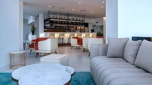 A modern living room with a sofa, coffee table, and chairs. There is a bookshelf and a desk in the background.