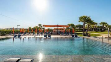 A swimming pool with lounge chairs and umbrellas, surrounded by palm trees and a clear sky.
