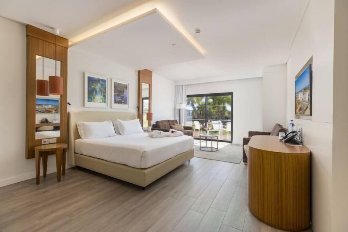 A modern hotel room with a bed, a desk, a chair, and a balcony with a view.