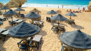 A beach with thatched umbrellas and lounge chairs, a sandy beach, and the ocean in the background.