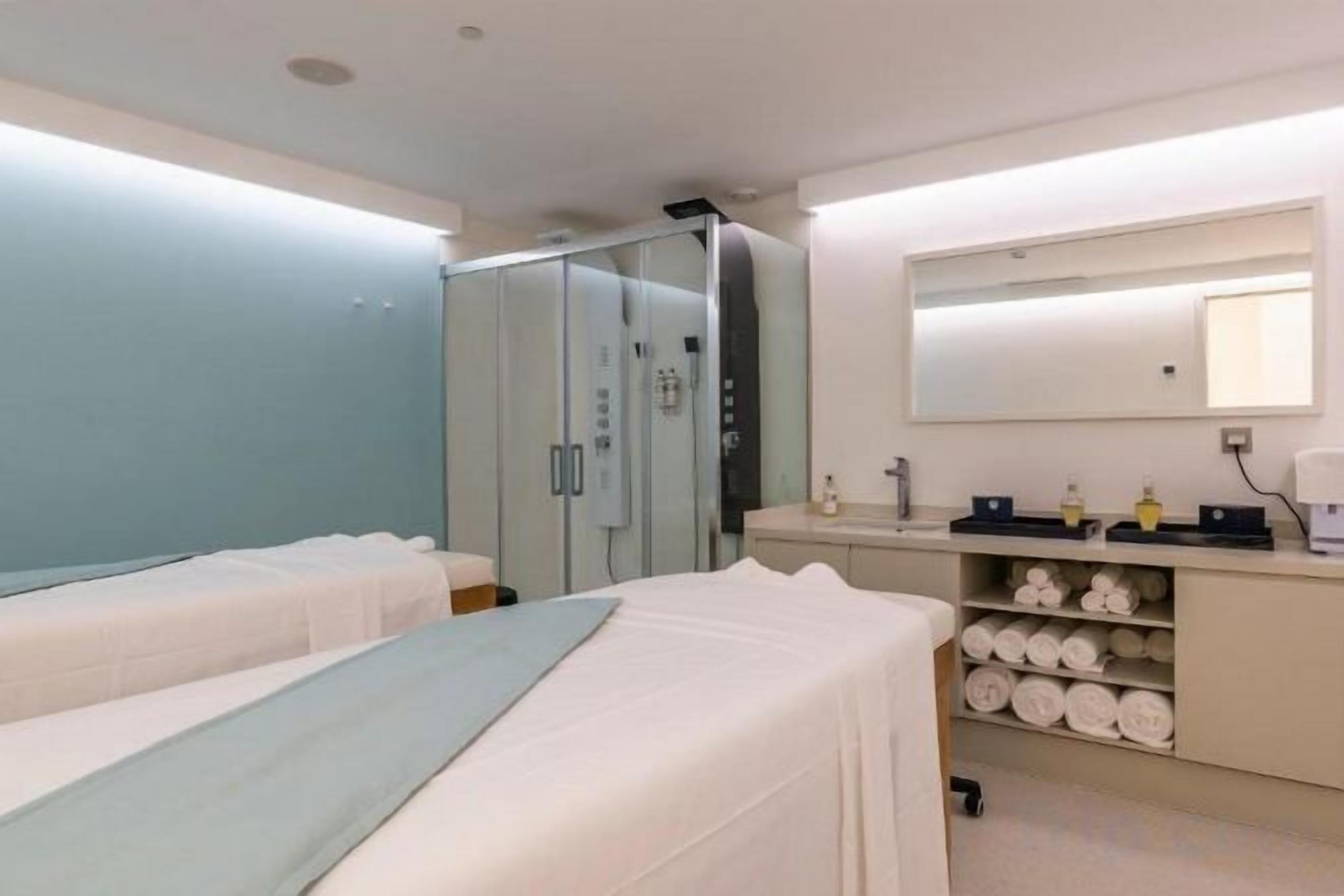 Habitació d'hotel amb dos llits, un armari encastat, un bany amb mirall i una estant amb productes de tocador.