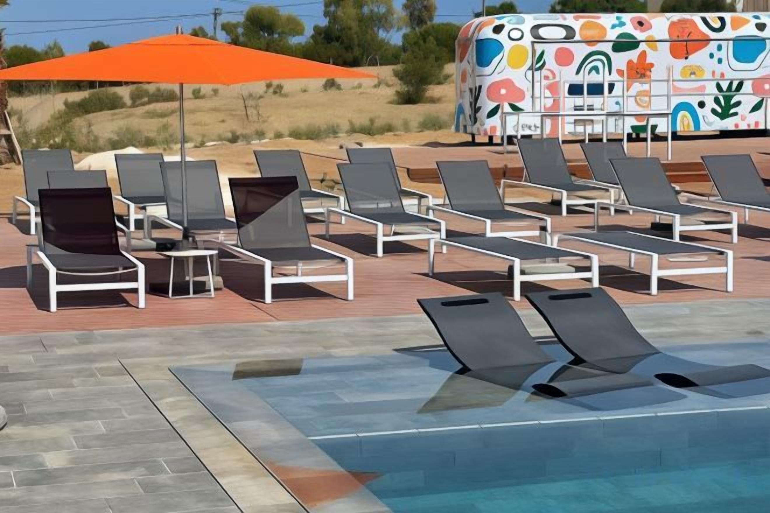 A pool area with lounge chairs and an orange umbrella.