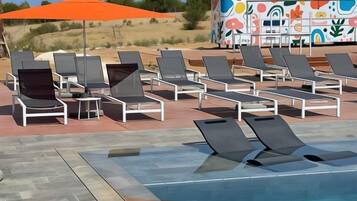 A pool area with lounge chairs and an orange umbrella.