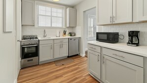A compact kitchen with white cabinets, a stove, microwave, and a coffee maker.