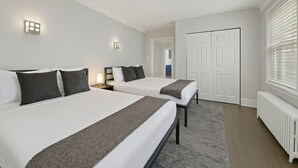 A hotel room with two beds, a white radiator, and a door with a white frame.