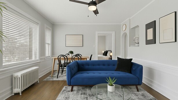 A living room with a blue sofa, a glass coffee table, and a ceiling fan.