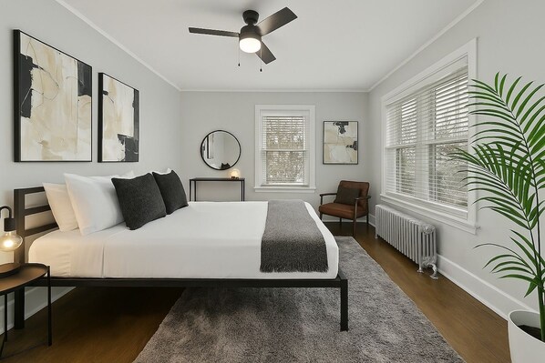 A bedroom with a bed, a ceiling fan, a radiator, a window with blinds, and a potted plant.