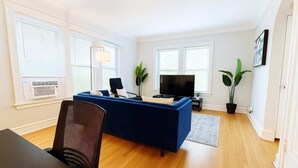 Una sala de estar moderna con un sofá azul, una silla negra, un televisor y dos plantas en macetas.