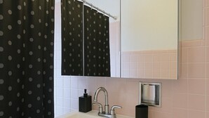 Et badeværelse med en hvid vask, et spejl over vasken, et toilet og en badegardine med sorte og hvide prikker.