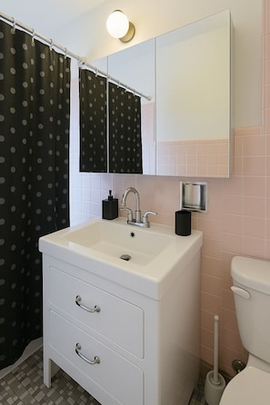 Een badkamer met een wit wastafel, een spiegel erboven, een toilet en een zwart-wit stippen douchegordijn.