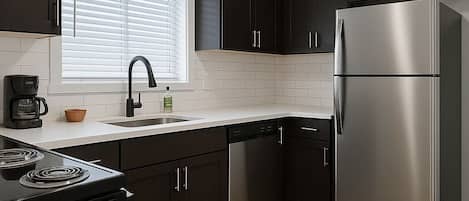 A modern kitchen with dark cabinets, stainless steel appliances, a black faucet, and a clock on the wall.